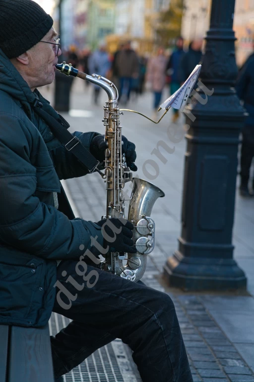 Уличный музыкант на оживленной улице. Саксофонист играет на центральной, пешеходной улице.