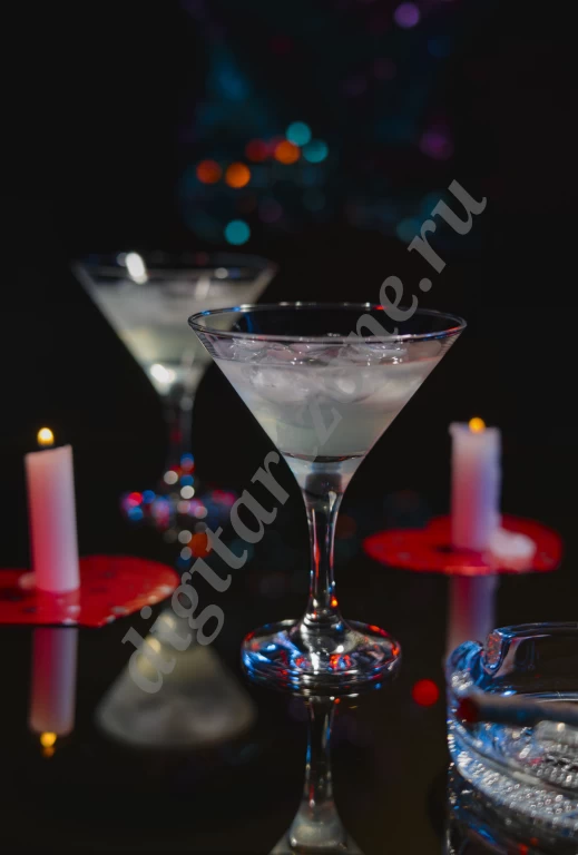 Два коктейльных бокала наполнены напитком со льдом. Рядом горят свечи на подставках в форме серде...