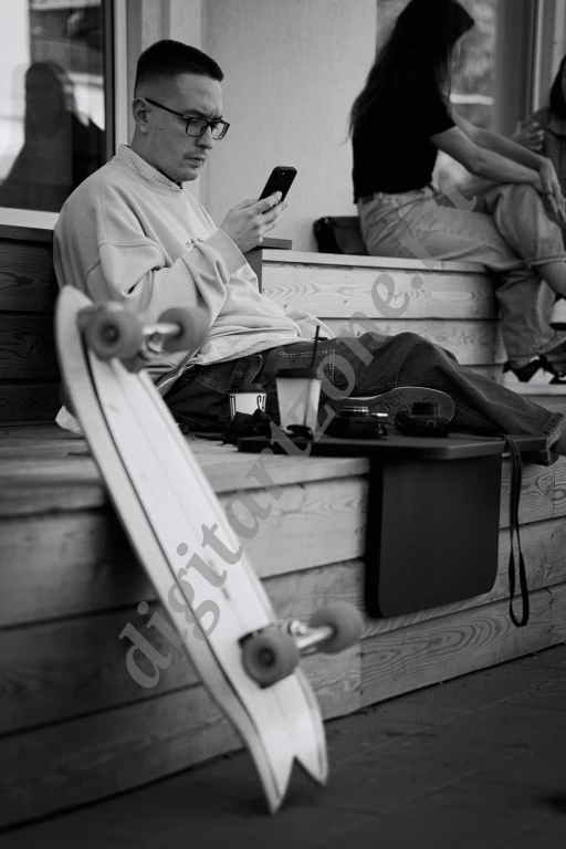 Черно белое фото, на котором запечатлен молодой мужчина со своим скейтбордом.  Молодой человек си...