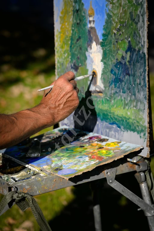 Художник пишет картину масляными красками. Рука художника, палитра, мольберт с установленным на н...