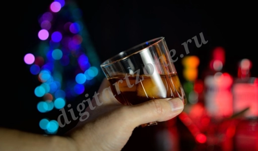 Стакан виски со льдом в протянутой руке на фоне барной стойки.