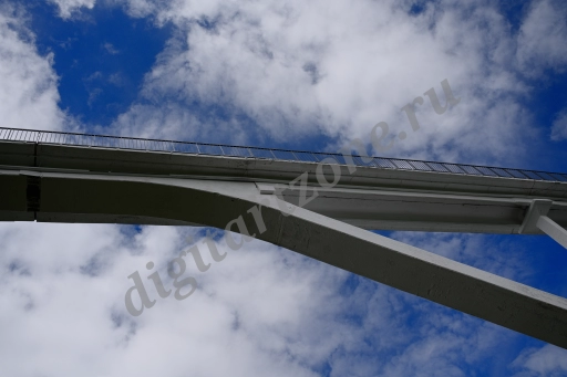 Пешеходный мост оригинальной архитектуры на фоне неба с облаками.